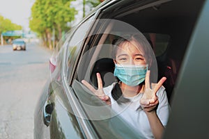 Asian teenager wearing protection mask sitting in car hand sigh for victory