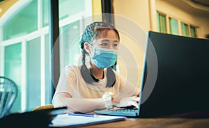 Asian teenager wearing protection mask working on computer laptop while covid-19 infected in bangkok thailand