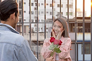 Asian teenager woman surprised and smiling at boyfriend gives red rose flowers at dinner in valentine day. young happy couple love