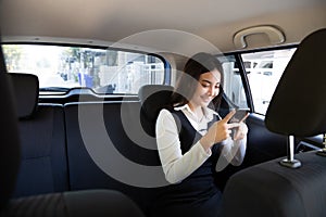 Asian teenager woman using a smartphone in back seat of car.