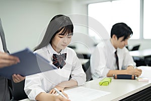 Asian teenagers in high school uniforms doing test in class