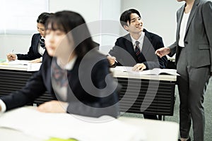 Asian teenagers in high school uniforms studying in class with teacher