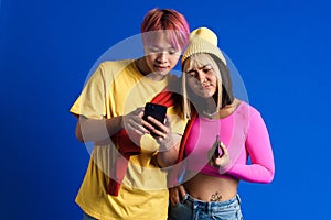 Asian teenagers with multicolored hair frowning while using cellphones