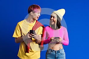 Asian teenagers with multicolored hair laughing while using cellphones