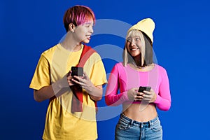 Asian teenagers with multicolored hair laughing while using cellphones