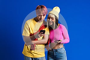 Asian teenagers with multicolored hair smiling while using cellphones