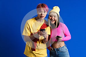 Asian teenagers with multicolored hair smiling while using cellphones