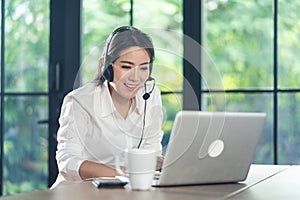 Asian Telemarketing or call center with headset working on computer lap top at home. Attractive Telesales talk and support remote