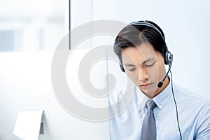 Asian telemarketing staff wearing headset concentrating on working in office