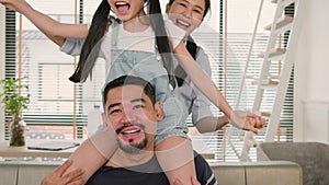 Asian Thai family together, dad plays and teases with daughter and mum by carrying and holding girl on shoulders in home living ro