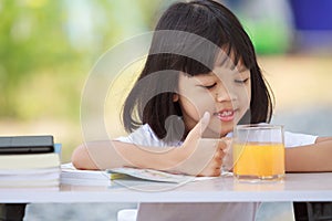 Asian Thai kid girl A cute face with a bright smile, wearing a white shirt, in good health. sitting outdoors There are books on