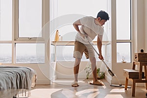 Asian Thai man using mop for cleaning floor in living room apartment, Man do household chores, housework concept.