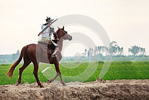 Asian Thai Warrior in traditional armor suit riding horse in rural farm background. Vintage Retro war costume concept