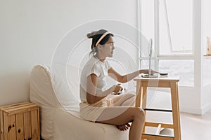 Asian Thai woman using pencil and drawing eyebrow, sitting on white couch in front of the mirror in room apartment
