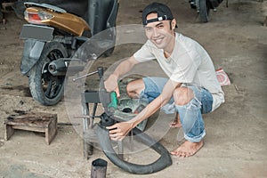 Asian tire repairman smiles into the camera while pouring fuel on a traditional press