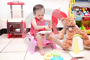 Asian toddler girl child sitting on potty and reading a book with toys & teddy bear, Potty training, Learning to use the Toilet