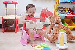 Asian toddler girl child sitting on potty and reading a book with toys & teddy bear, Potty training, Learning to use the Toilet