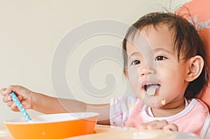 Asian toddler girl eating cereals with milk on high chair at home
