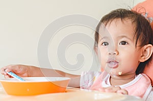 Asian toddler girl eating cereals with milk on high chair at home