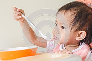 Asian toddler girl eating cereals with milk on high chair at home