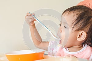 Asian toddler girl eating cereals with milk on high chair at home