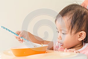 Asian toddler girl eating cereals with milk on high chair at home