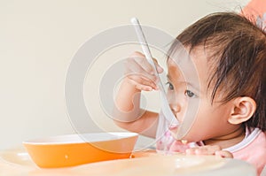 Asian toddler girl eating cereals with milk on high chair at home