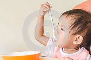 Asian toddler girl eating cereals with milk on high chair at home