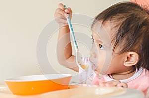 Asian toddler girl eating cereals with milk on high chair at home