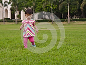 Asian toddler is learning to walk step by step on greeny grass.