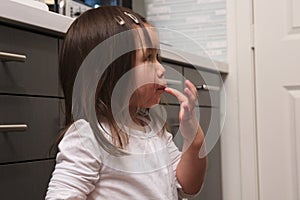 Asian toddler licking icing off finger