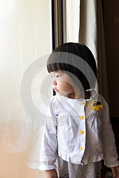 Asian toddler watching the rain through window