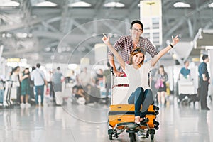 Asian tourist couple happy and excited together for the trip, girlfriend sitting and cheering on baggage trolley or luggage cart