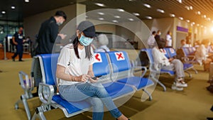 Asian tourist with mobile phone ,wearing hygienic mask, sit on chair with social distancing to prevent pandemic during travel