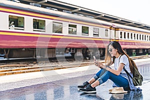 Asian tourist teenage girl at train station using smartphone map, social media check-in, or buy ticket booking