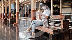 Asian tourist teenage girl wearing mask waiting distance train station using smartphone, social media check-in, lone