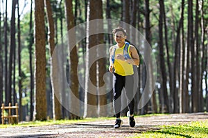 Asian trail runner is running outdoor in the pine forest dirt road with water backpack for exercise activities training to race in