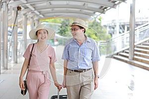 Asian traveler couple husband and wife in pink and blue shirt with white nice hat and luggage walking in downtown with happy