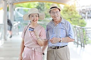 Asian traveler couple husband and wife in pink and blue shirt with white nice hat and luggage walking in downtown with happy