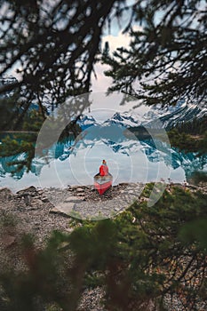 Asian traveler in red jacket sitting on canoe by the lakeside in Spirit Island located in Maligne Lake at Jasper national park