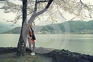 Asian traveler woman standing under branches of pink flower japanese cherry tree.