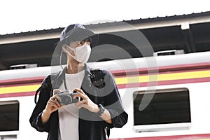 Asian travelers men and camera in train station with medical face mask to protection the Covid-19, new normal lifestyle