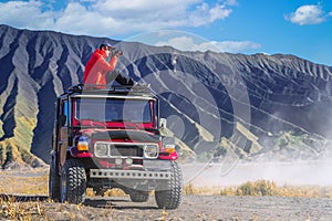 Asian traveller take a photo on the top of advanture car in bromo volcano mountain