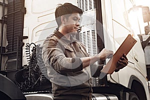 Asian a truck driver holding clipboard inspecting safety maintenance checklist of semi truck.