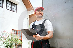 Asian truck driver wearing red cap holding a clipboard, checking the delivery packages checklists or paperwork and standing.