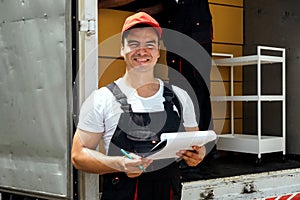 Asian truck driver wearing red cap holding a clipboard, checking the delivery packages checklists or paperwork and standing.