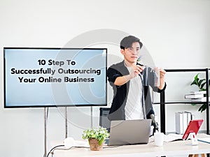 Asian tutor man use face shield before share education lesson on television screen about 10 step to successfully outsourcing your