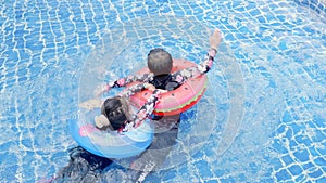 Asian two children little girls and boy playing in outdoor swimming pool on inflatable toy ring