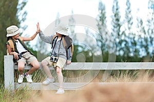 Asian two children raise give me five and sitting on the white fence outdoors, adventure and tourism for destination and leisure t