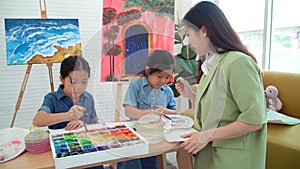 Asian two siblings learning study watercolor paint together at home. Teacher or parent teach student or daughter drawing paint